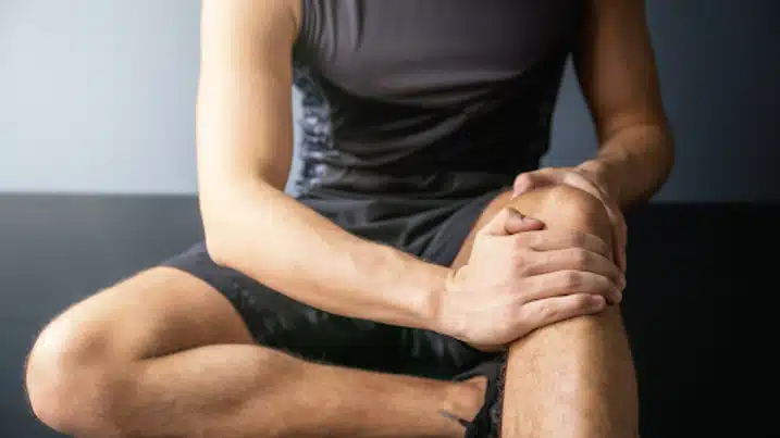Extremity Joint Care, Male sitting on ground in workout clothes, grabbing knee in pain