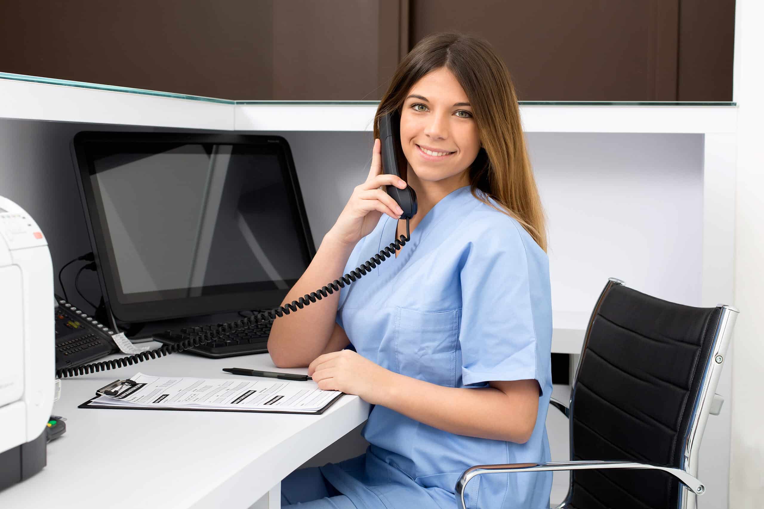Female Nurse answering phone at desk with computer